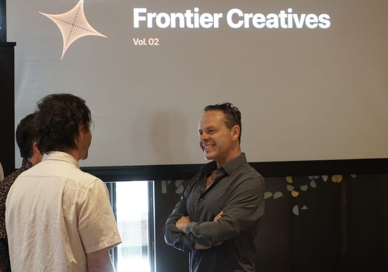 Two attendees talking in front of the projected Frontier Creatives Vol. 02 title card.