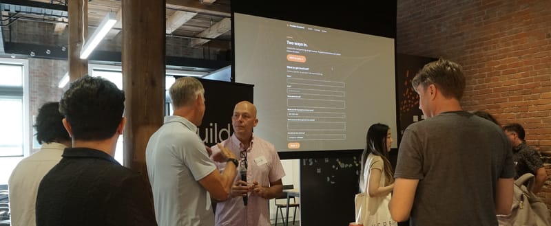 Attendees standing and talking while the Frontier Creatives contact page is projected behind them.