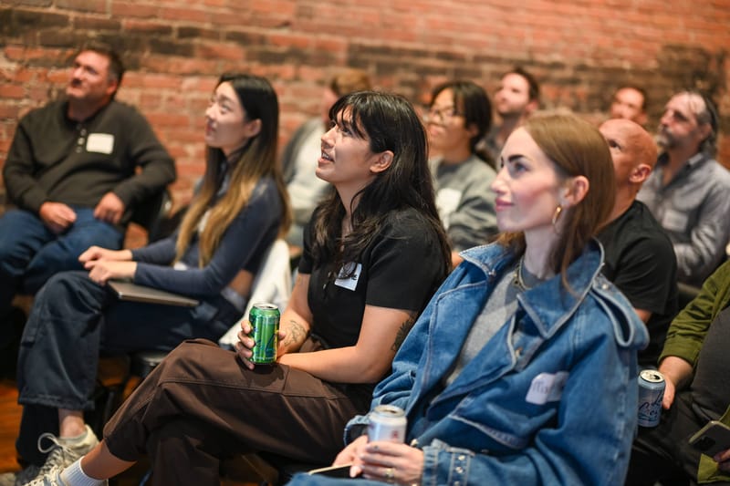 Attendees seated in the front rows looking toward the stage, brick wall behind them.