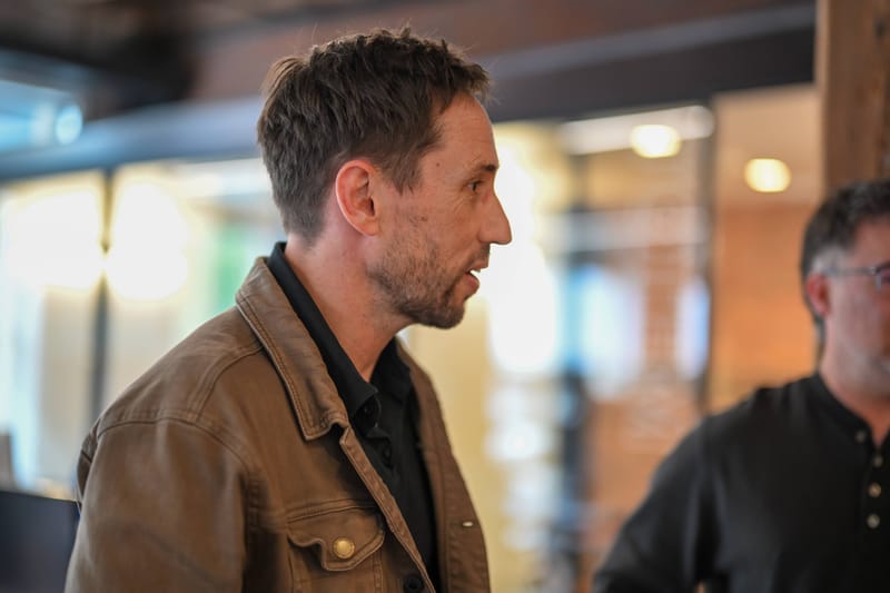 An attendee in a tan jacket in profile, listening during a talk.