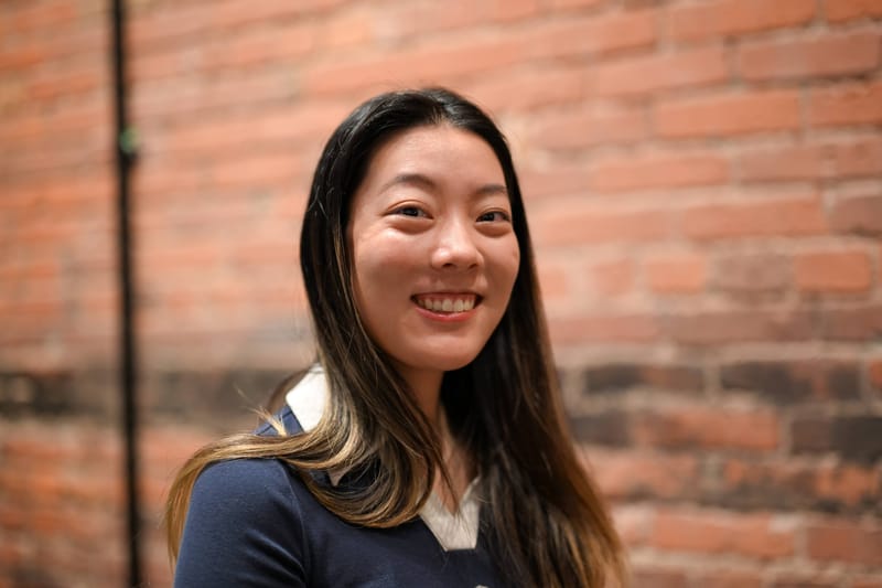 Yilin Zhu smiling in front of a brick wall.