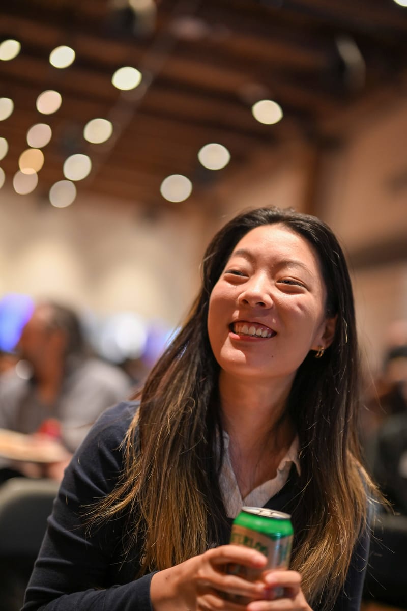 Yilin Zhu laughing and holding a drink, warm string lights behind her.