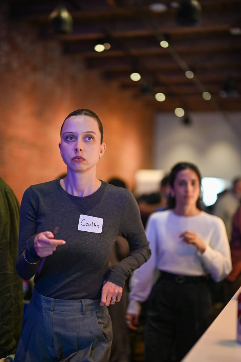 An attendee in a name tag gesturing mid-conversation, others in the background.