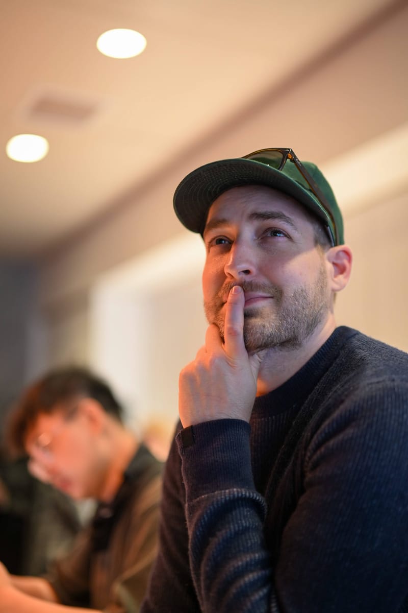Stephen Sherwood in a cap, hand to his chin, listening during a talk.