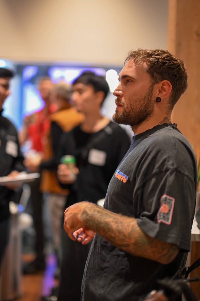 An attendee in a printed tee talking, drink in hand, with others behind him.