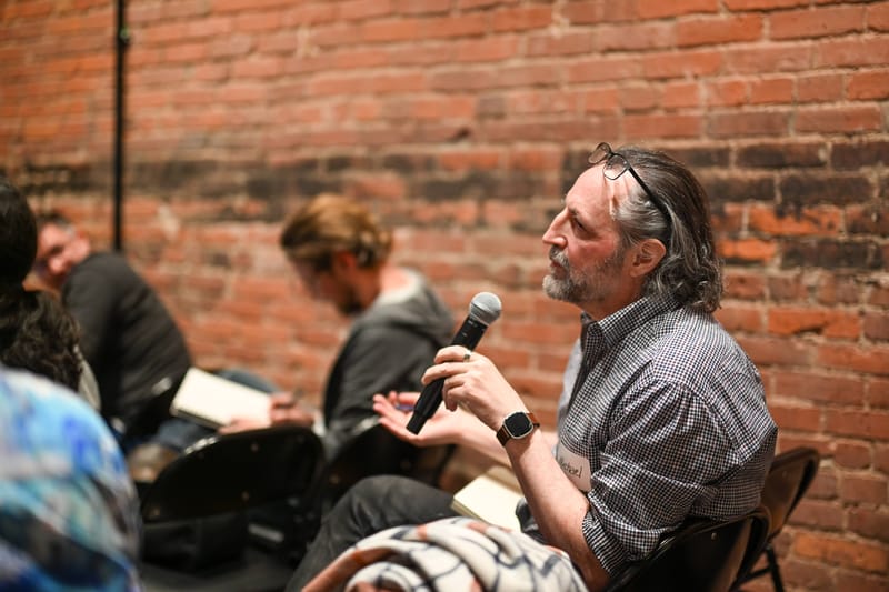 An attendee standing with a microphone asking a question from the side of the room.