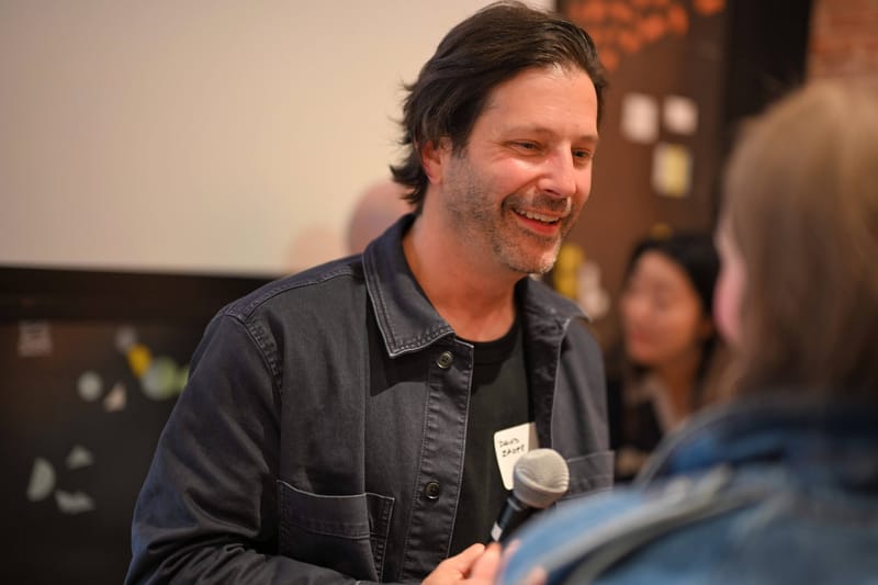 David Zager holding a microphone mid-sentence, talking with an attendee.