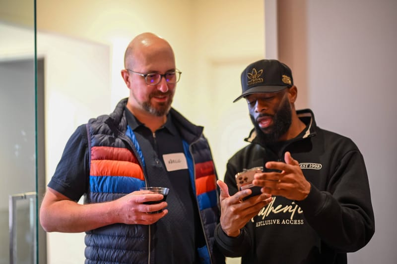Two attendees talking with drinks in hand beside a doorway.