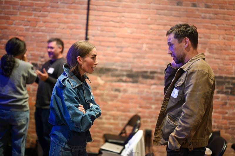 Two attendees talking beside the exposed brick wall as the room empties.