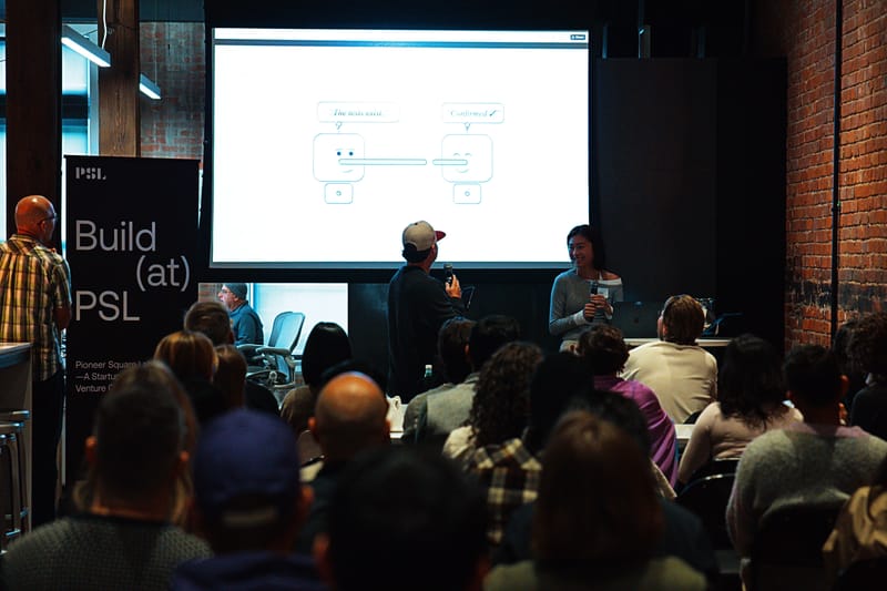 A presenter at the front of the room with a projected flow diagram, a seated audience in the foreground.