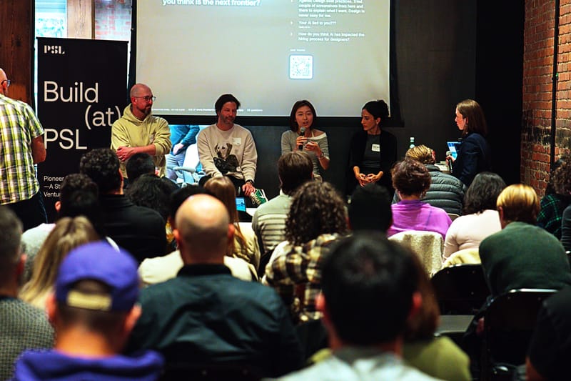 Five panelists seated at the front of the room with a projected list of audience questions behind them, viewed over the audience.