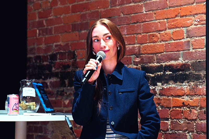 The moderator seated against a brick wall, microphone in hand, looking up with a smile.