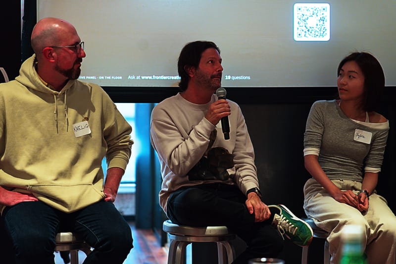 Three panelists on stools, the QR code for the question board projected above them.
