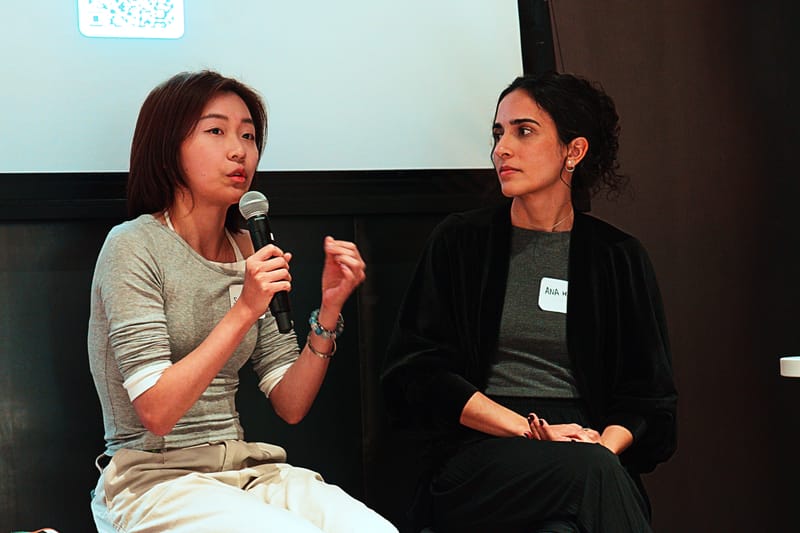 Two panelists seated side by side, one speaking into a microphone and gesturing.