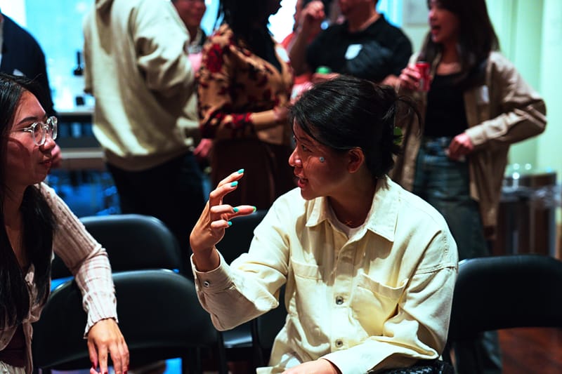 Attendees in conversation across a row of black chairs, one gesturing mid-sentence.